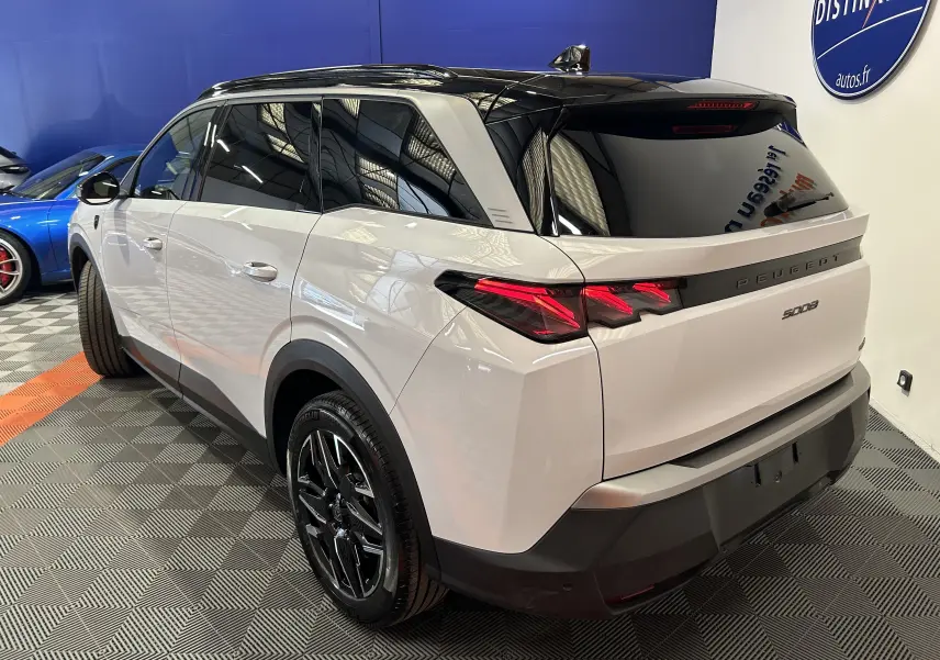 Vue 3/4 arrière droit d’un Peugeot 5008 blanc avec toit noir et feux arrière LED distinctifs en intérieur showroom.
