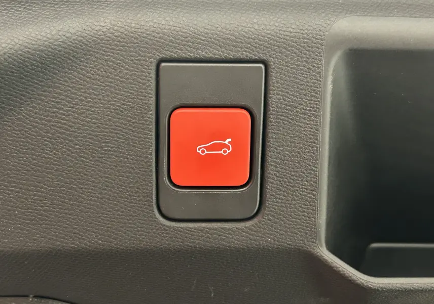 Bouton rouge d'ouverture électrique du hayon sur tableau de bord noir d'un Peugeot 5008 blanc hybride 2025.