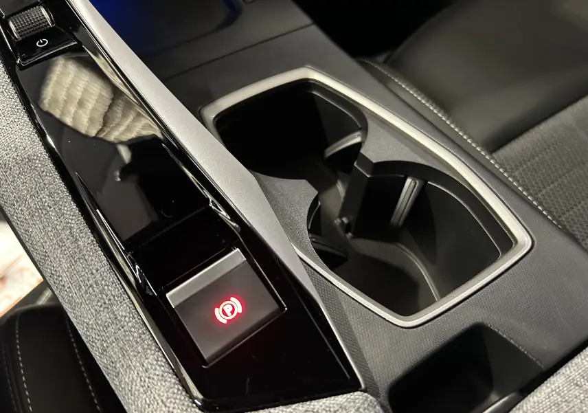 Gros plan sur la console centrale noire et grise avec porte-gobelets et bouton frein à main électrique allumé du Peugeot 5008 blanc.