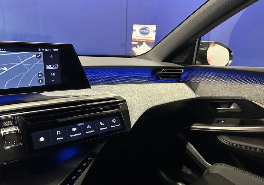 Vue intérieure côté passager du Peugeot 5008 Hybrid 2025, avec éclairage d'ambiance bleu et tableau de bord moderne.