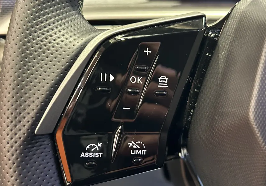 Gros plan sur les commandes noires du volant côté gauche du Peugeot 5008 Hybrid blanc, avec boutons d'assistance et limitation.