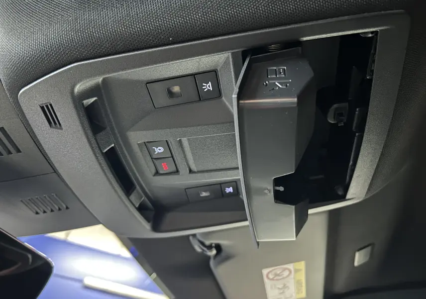 Vue en gros plan du panneau de commandes au plafond intérieur du Peugeot 5008 Hybrid blanc, avec compartiment ouvert et boutons lumineux.