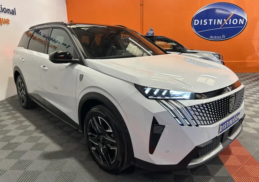 Vue 3/4 avant d’un Peugeot 5008 Hybrid blanc avec toit noir et phares LED allumés en intérieur showroom.