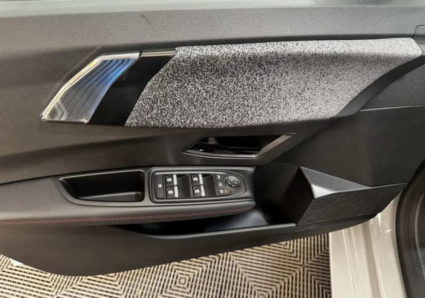 Détail de la porte avant gauche de la Renault Clio gris clair 2026 avec commandes électriques et insert décoratif texturé.