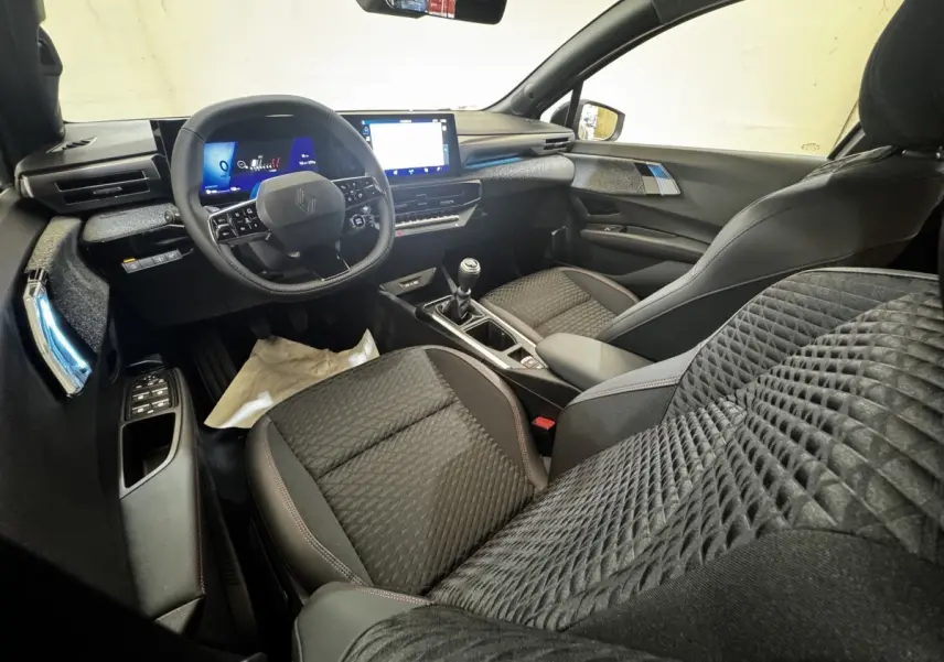 Vue intérieure avant droite de la Renault Clio Techno TCe 115 essence 2026 avec sièges noirs et tableau de bord numérique.