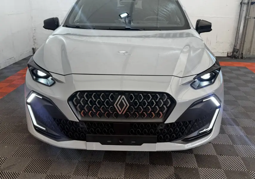 Vue frontale d'une Renault Clio gris clair 2026 avec feux LED allumés et calandre hexagonale distinctive.