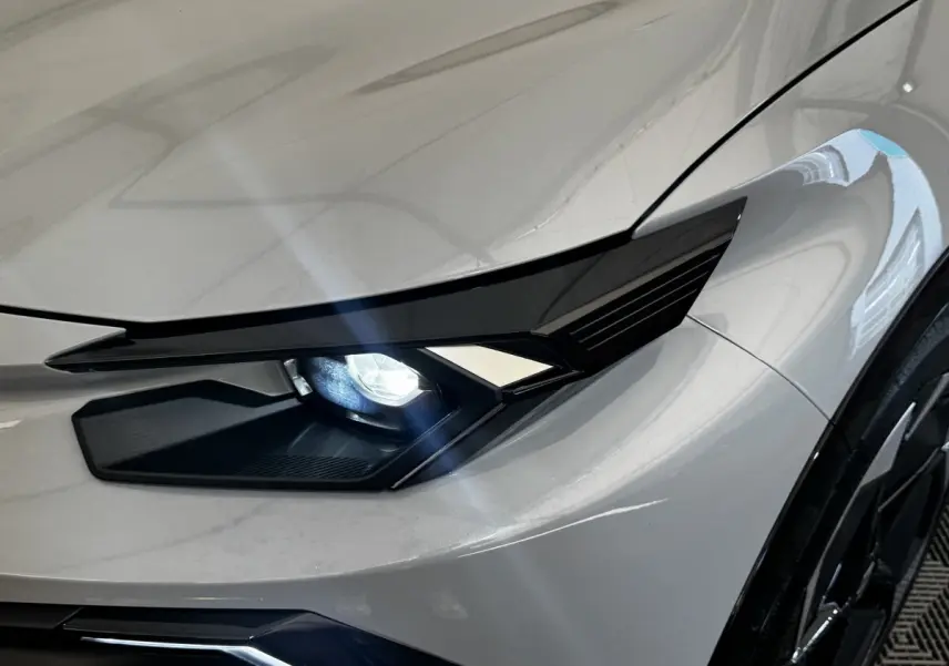 Gros plan sur le phare avant droit allumé d'une Renault Clio 2026 gris clair avec carrosserie lisse et jante noire.