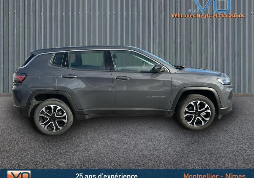 Profil côté gauche du Jeep Compass gris 2024 garé devant un mur métallique, roues alliage visibles.