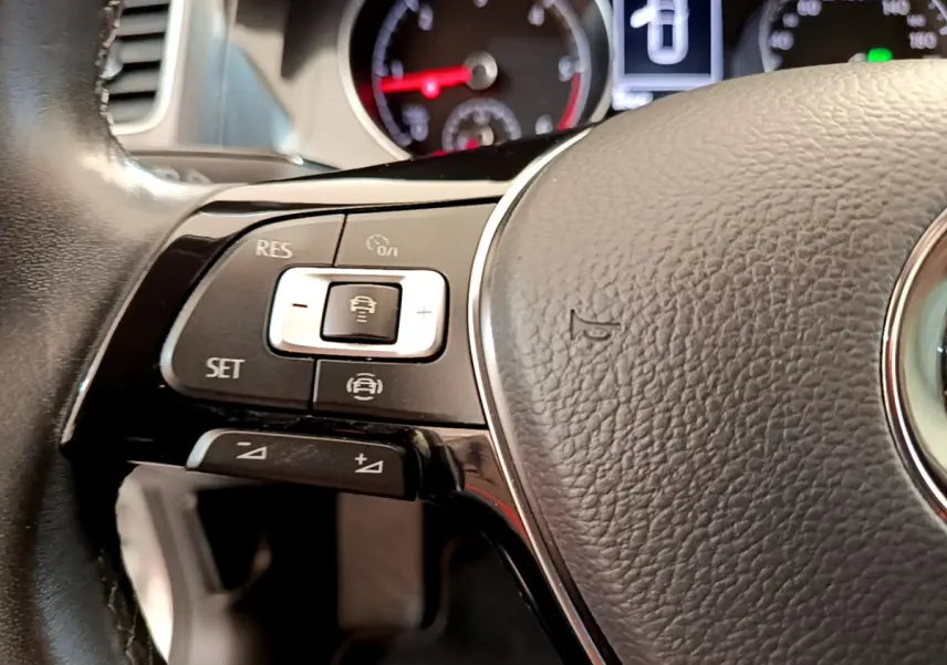 Gros plan sur la partie gauche du volant cuir de la Volkswagen Golf gris clair, avec commandes de régulateur adaptatif visibles.