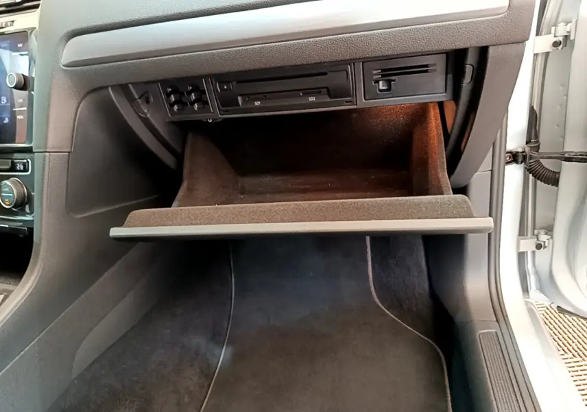 Gros plan sur la boîte à gants ouverte côté passager d'une Volkswagen Golf gris clair 2019, intérieur noir.