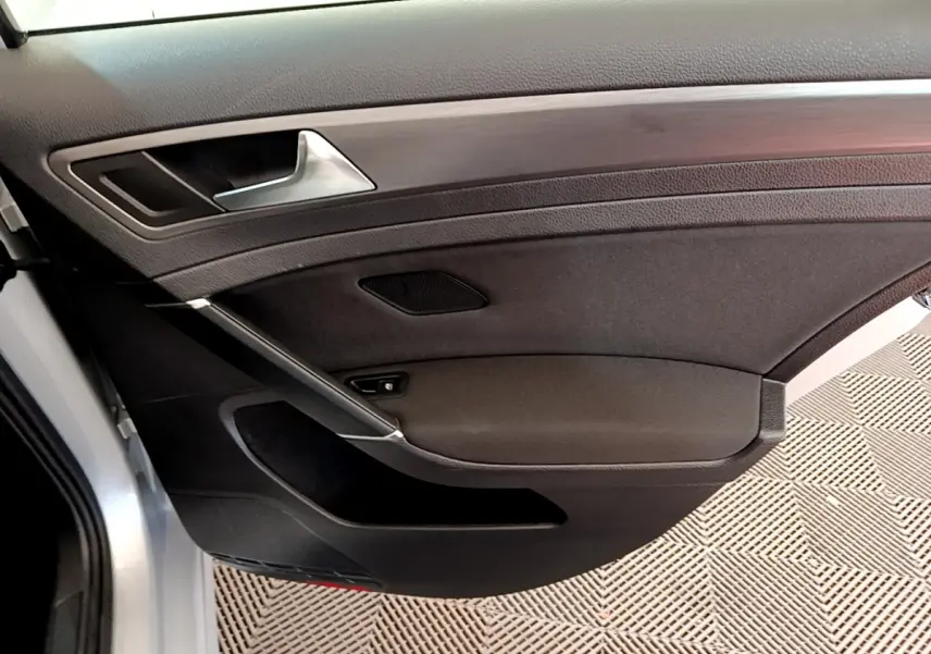 Vue rapprochée de la porte avant gauche intérieure de la Volkswagen Golf gris clair avec poignée argentée et garniture noire.