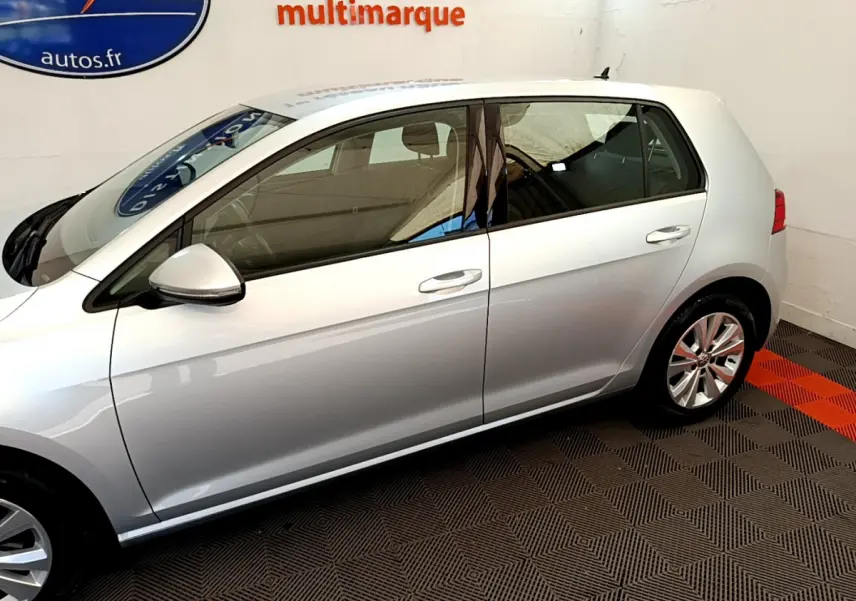 Profil côté gauche d'une Volkswagen Golf gris clair 2019 garée en intérieur sur sol damier noir et rouge