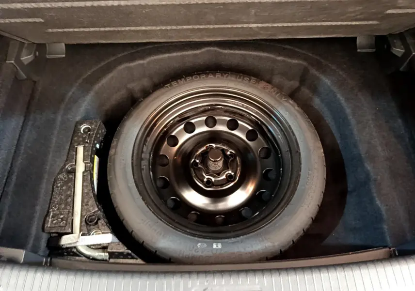 Roue de secours galette noire dans le coffre d'une Volkswagen Golf gris clair, vue plongeante sur le rangement.