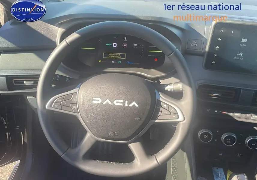 Vue intérieure centrée sur le volant DACIA noir avec tableau de bord digital et écran tactile à droite.