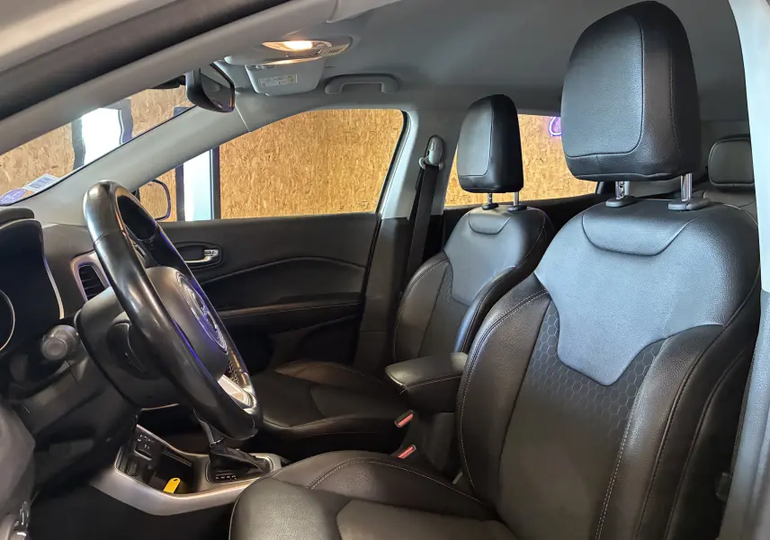 Vue intérieure côté conducteur du Jeep Compass 2021, sièges cuir noirs avec accoudoir central et volant multifonctions.