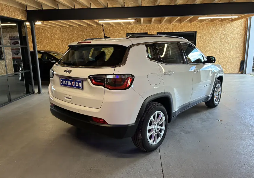 Vue 3/4 arrière droite du Jeep Compass ivoire avec barres de toit et jantes alu dans un garage.