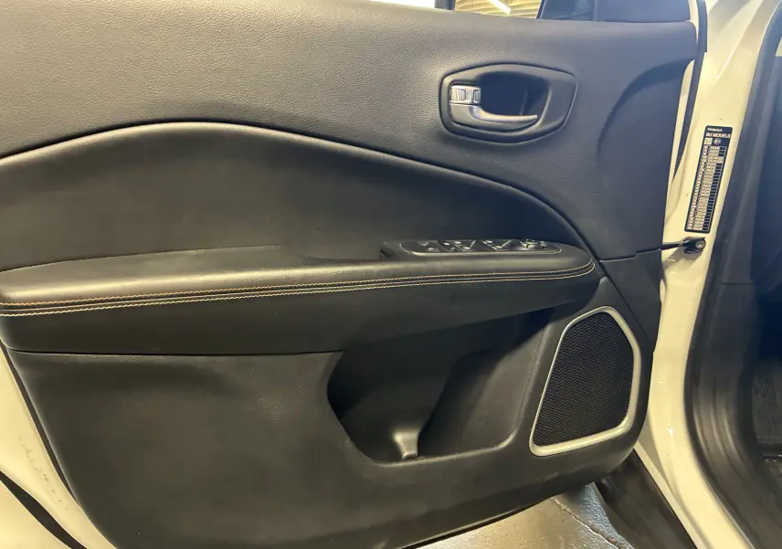 Vue intérieure côté gauche de la porte avant ivoire du Jeep Compass 2021 avec commandes vitres et haut-parleur intégré.