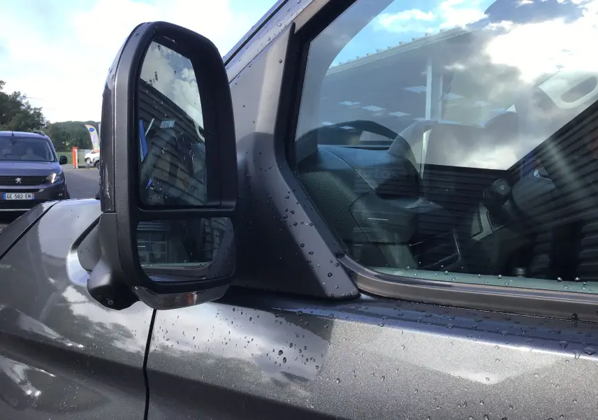 Rétroviseur latéral gauche en gros plan du Volkswagen Transporter ProCab gris anthracite avec gouttes d'eau sur la carrosserie.