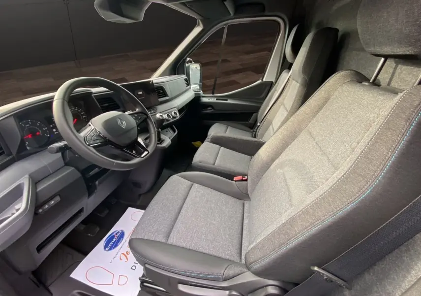 Vue intérieure côté conducteur du Renault Master 2025, sièges gris tissu avec surpiqûres bleues et tableau de bord noir.