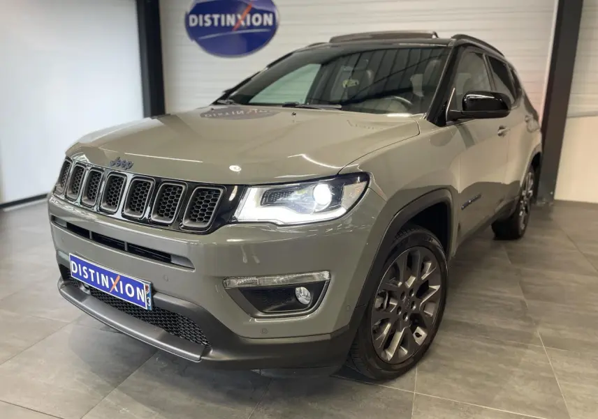 Jeep Compass gris foncé vu en 3/4 avant droit avec phares allumés et jantes alliage sombres.