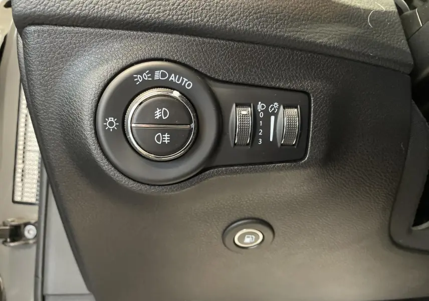 Gros plan sur les commandes d'éclairage et l'ouverture de trappe à carburant du tableau de bord noir d'un Jeep Compass Trailhawk.