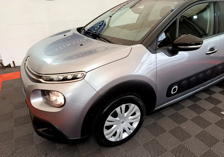 Citroën C3 gris clair vue 3/4 avant droit, avec protections latérales noires et jantes argentées.