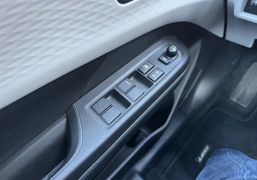 Gros plan sur la commande des vitres et rétroviseurs côté gauche de la porte intérieure d'une Suzuki Swift 2024 blanc/gris.