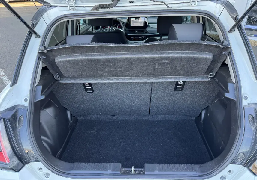 Coffre ouvert vu de l'arrière d'une Suzuki Swift 1.2 Dualjet Pack Auto Hybride blanc/gris, intérieur noir visible.