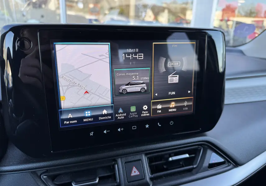 Écran tactile central de la Suzuki Swift 2024 affichant navigation, consommation hybride et radio FM en intérieur.