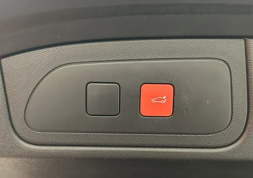 Gros plan sur les boutons de commande du hayon électrique, avec un bouton rouge illustrant un coffre ouvert, intérieur noir.