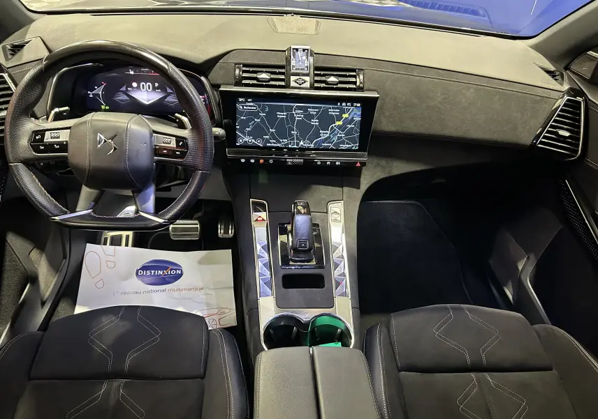 Vue intérieure avant du DS7 gris titane 2024, mettant en valeur le volant multifonction et l'écran tactile central avec navigation.