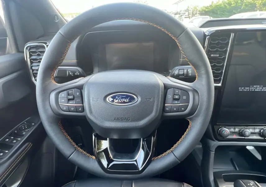 Volant cuir noir avec surpiqûres marron et commandes multifonctions du Ford Ranger 2025, tableau de bord et écran tactile visibles.