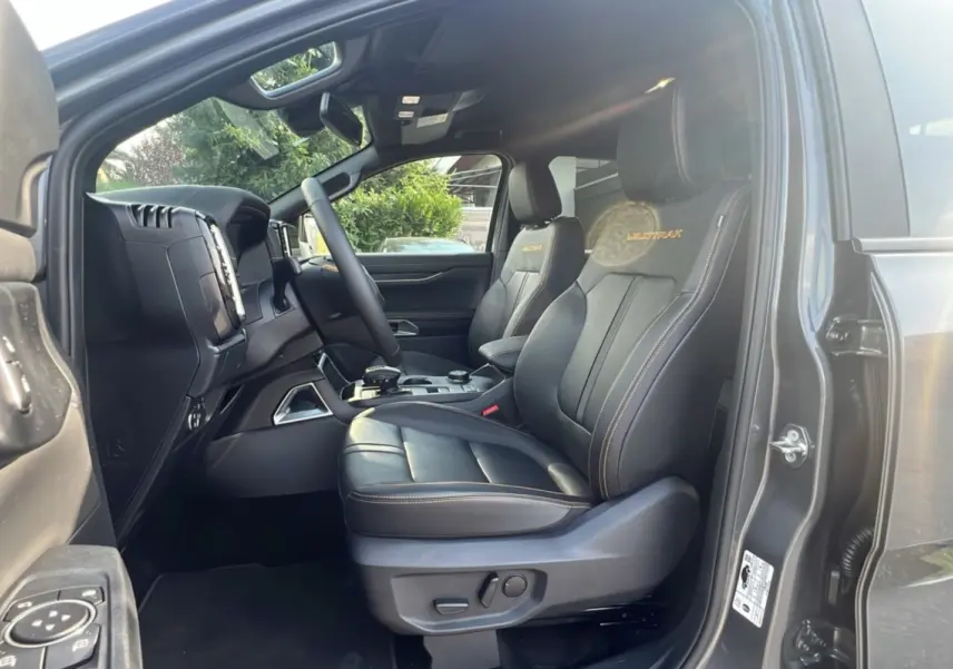 Intérieur côté conducteur du Ford Ranger Wildtrak gris carbone, sièges cuir noirs avec surpiqûres orange et logo Wildtrak.