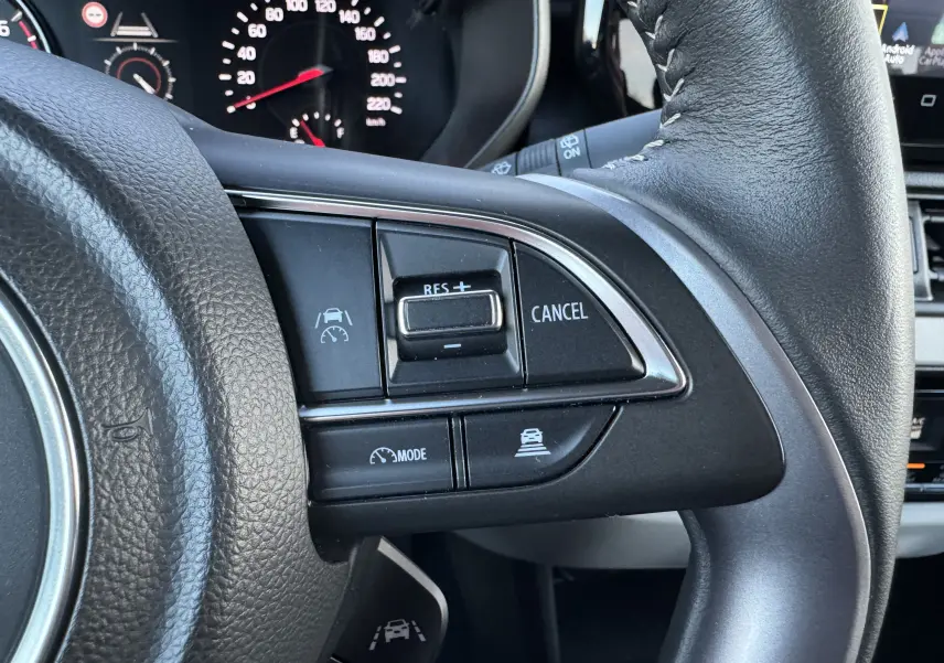 Gros plan sur les commandes de régulateur de vitesse au volant cuir noir de la Suzuki Swift blanche 2025 hybride.