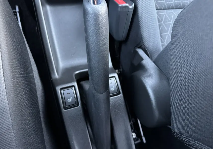 Gros plan sur le frein à main et les boutons de sièges chauffants noirs entre les sièges avant d'une Suzuki Swift blanche.