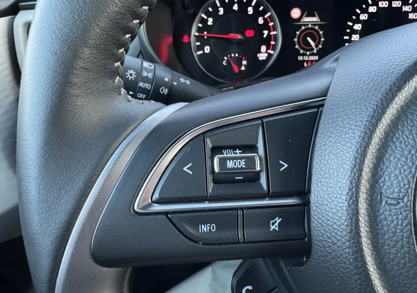 Gros plan sur les commandes audio au volant à gauche de la Suzuki Swift 1.2 Privilège Hybrid 2025 avec tableau de bord en arrière-plan.