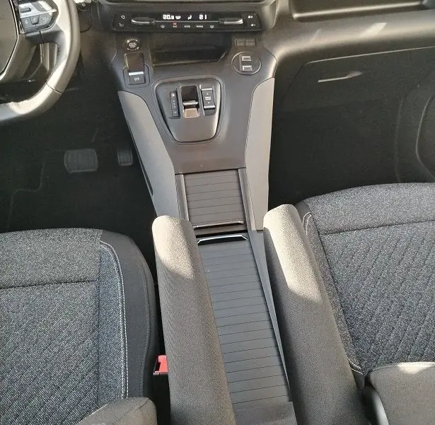 Vue intérieure centrée sur la console centrale et levier de vitesse du Peugeot Rifter 2025, sièges gris foncé visibles.