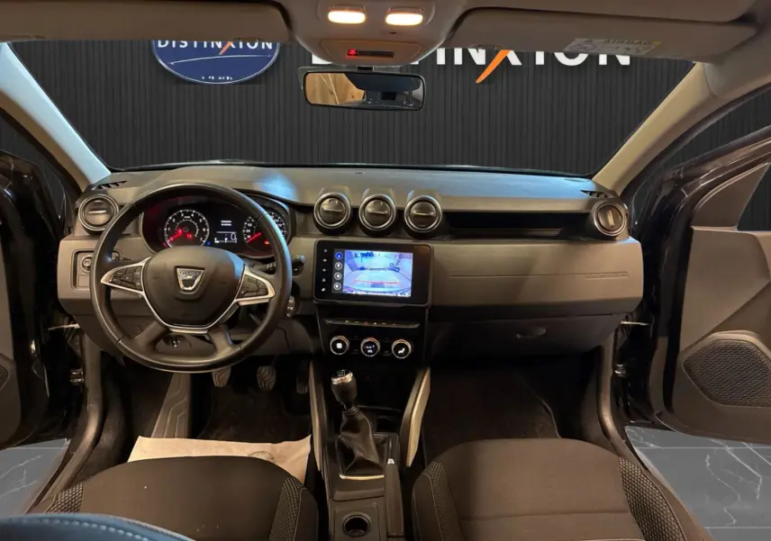 Vue intérieure avant du Dacia Duster noir 2022, montrant le tableau de bord avec écran tactile et volant multifonction.