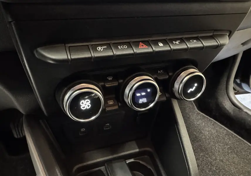 Gros plan sur la console centrale du Dacia Duster 2022 noire, montrant les commandes de climatisation et les boutons de fonction.