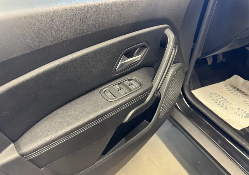 Vue rapprochée de la porte avant gauche noire du Dacia Duster 2022, montrant les commandes électriques des vitres et la poignée.