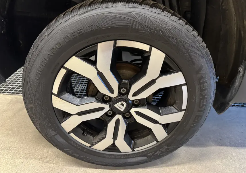 Gros plan sur la jante bicolore en alliage du Dacia Duster noir, mettant en valeur le design moderne et le logo central.