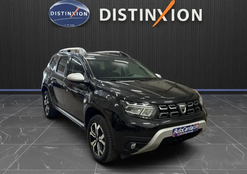 Dacia Duster noir en 3/4 avant droit, avec rétroviseurs blancs et jantes bi-ton, sur fond intérieur showroom.