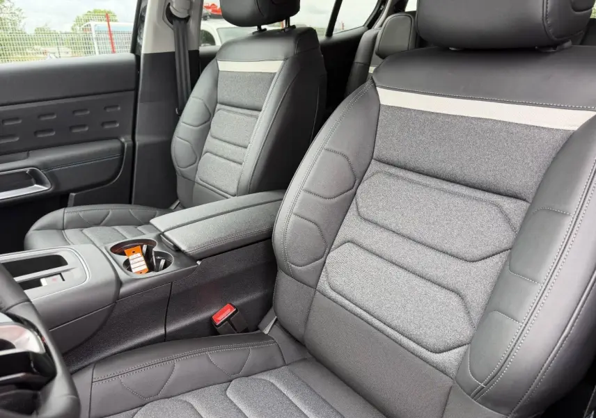 Vue rapprochée des sièges avant gris tissu et cuir du Citroën C5 Aircross 2025, avec accoudoir central et console.