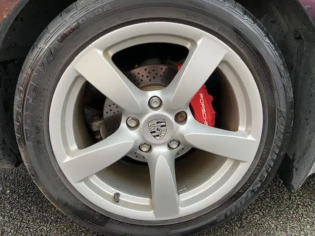 Gros plan sur la jante argentée d’une Porsche Cayman noire de 2008, avec étrier de frein rouge marqué Porsche.