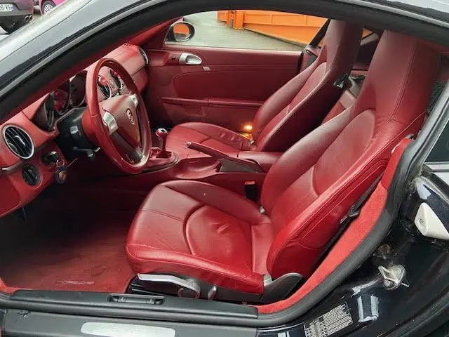 Intérieur rouge de la Porsche Cayman 2.7L 245CV 2008 vu côté gauche, sièges cuir et tableau de bord élégants.