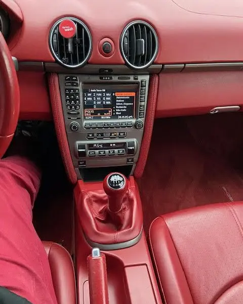 Intérieur rouge vif du Porsche Cayman 2.7L 2008, vue centrée sur la console avec levier de vitesse manuel et tableau de bord numérique.