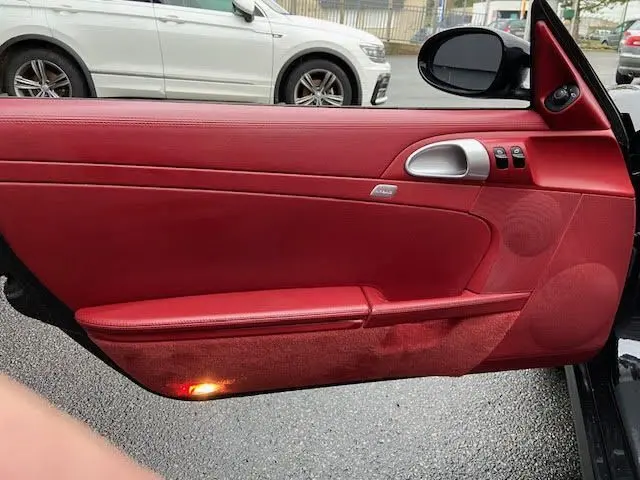 Vue intérieure de la porte côté conducteur d'une Porsche Cayman noire de 2008 avec garniture cuir rouge et éclairage bas.