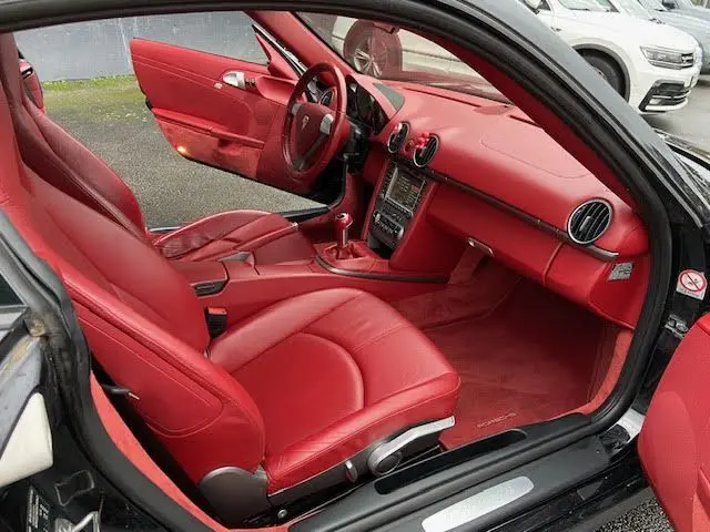 Intérieur rouge vif d'une Porsche Cayman 2.7L 245CV 2008, vue côté conducteur avec volant et sièges en cuir.