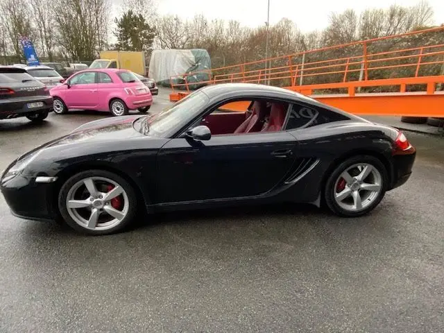 Profil droit d'une Porsche Cayman noire de 2008 avec intérieur cuir rouge et jantes alliage cinq branches.