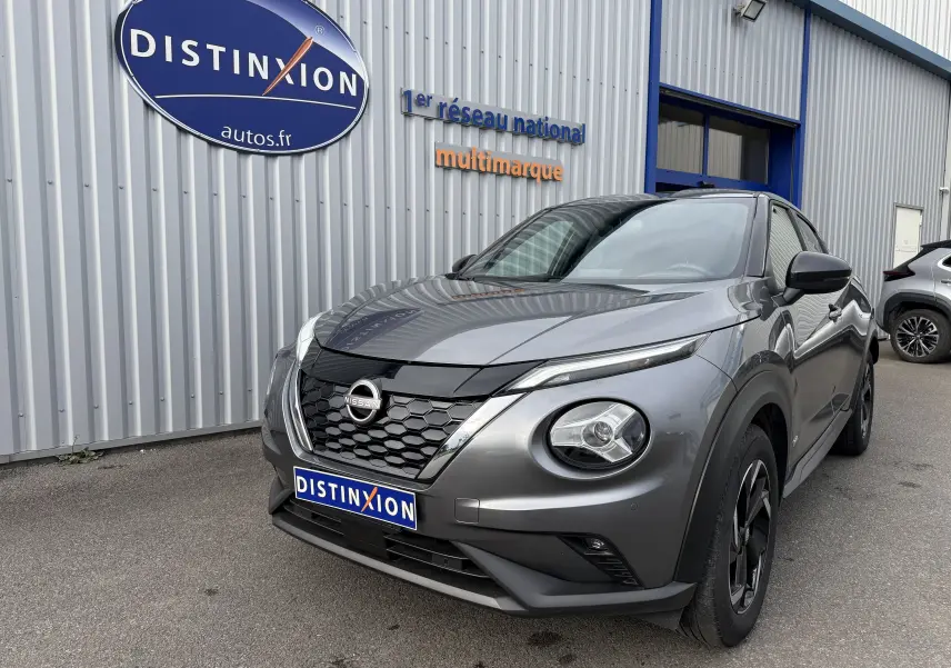 Nissan Juke 1.6 HEV gris squale métal en 3/4 avant droit, avec calandre noire et phares ronds distinctifs.